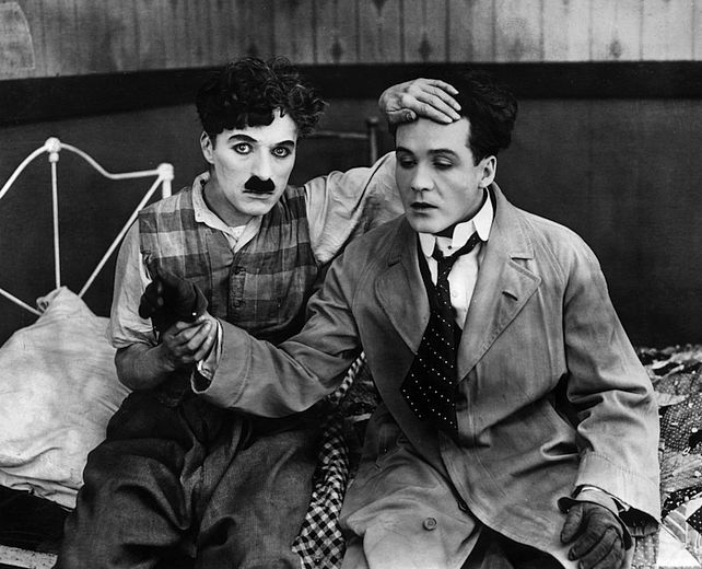 Charlie Chaplin tupft einem Mann das Gesicht ab.