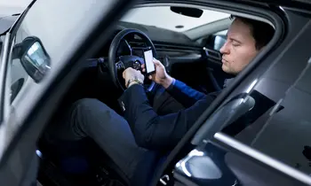 Ein Mann sitzt in einem Auto und schaut auf sein Smartphone.